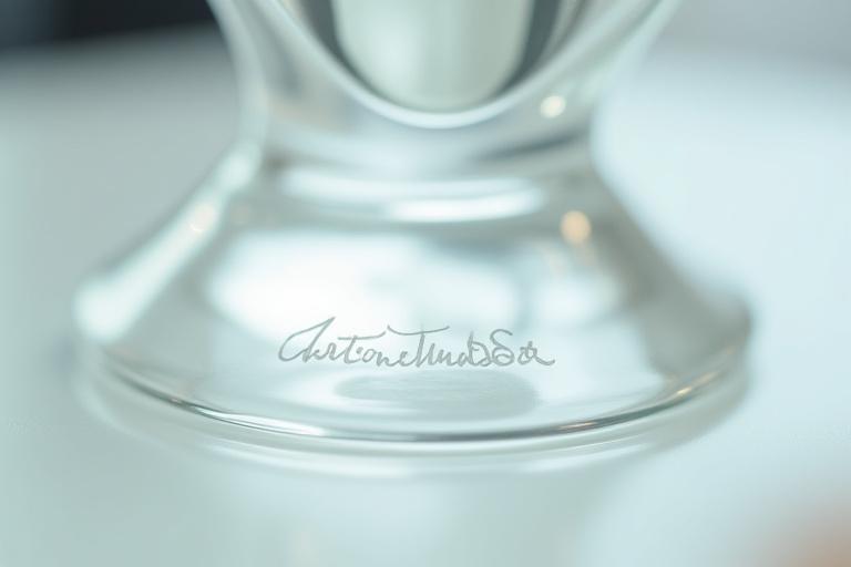 Close-up of an etched artisan signature on the base of a clear glass sculpture